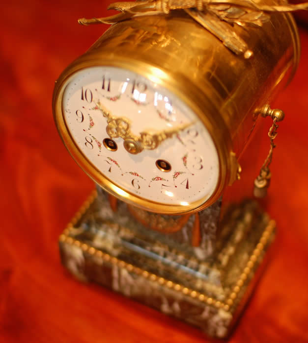A French mantel clock on a Marble base which has Ormalu decorations , the clock is of 8 day duration , striking hourly and half hourly on a bell with a white convex enamel dial showing arabic Numerals and garlands of flowers with finely pierced Gilded Brass Hands and a cast brass bezel surround . A small clock which would fit most mantels or perhaps even a 'Boudoir' ! . Made in Paris around 1890