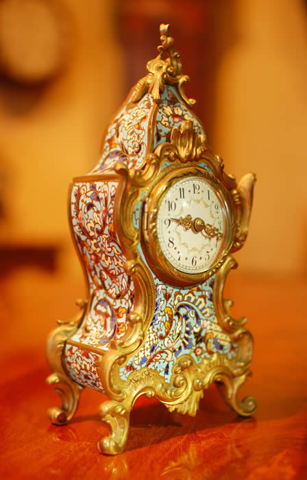 A small , decorative , timepiece mantel clock with a convex enamelled dial showing arabic numerals and garlands of flowers . The case is Cloisonne with raised gilt 'C' scrolls. A superb small time-piece and sold with a full 12 month , RTB Guarantee . 