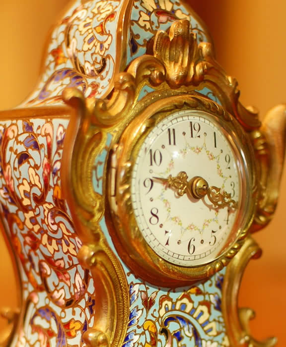 A small , decorative , timepiece mantel clock with a convex enamelled dial showing arabic numerals and garlands of flowers . The case is Cloisonne with raised gilt 'C' scrolls. A superb small time-piece and sold with a full 12 month , RTB Guarantee . 