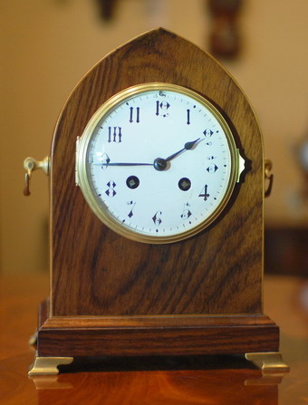 A French 'Lancet Top' mantel clock of 8 day duration , striking hourly and half hourly on a gong , a white convex enamel dial showing Gothic style Numerals polished blued steel Hands and a Cast brass bezel surround . The Rosewood case has a n inlaid edge in Boxwood with polished brass bracket feet and rear locking door , made in Paris around 1890
