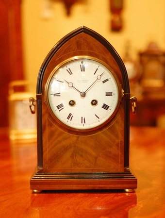 A French 'Lancet Top' mantel clock of 8 day duration , striking hourly and half hourly on a gong , a white convex enamel dial showing Roman Numerals polished blued steel Hands and a Cast brass bezel surround . The case has a good level of detail with a reeded canted edge leading to the Lancet arch  being ebonised and offering a good contrast to the flame Mahogany ,standing on bun feet and rear locking door , made in Paris around 1890 Stamped Maroue . 