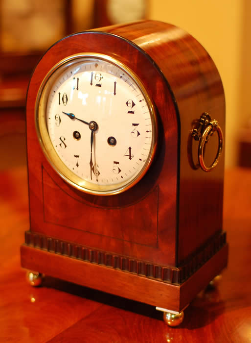 A French 8 day mantel clock , striking the hours and the half hours on a gong . A white enamel dial with arabic numerals . The case in mahogany with inlays of ebony and decorative brass handles to the sides . The rear door is glazed . Standing on polished brass ball feet . (see close up pictures) . Circa 1870-80
