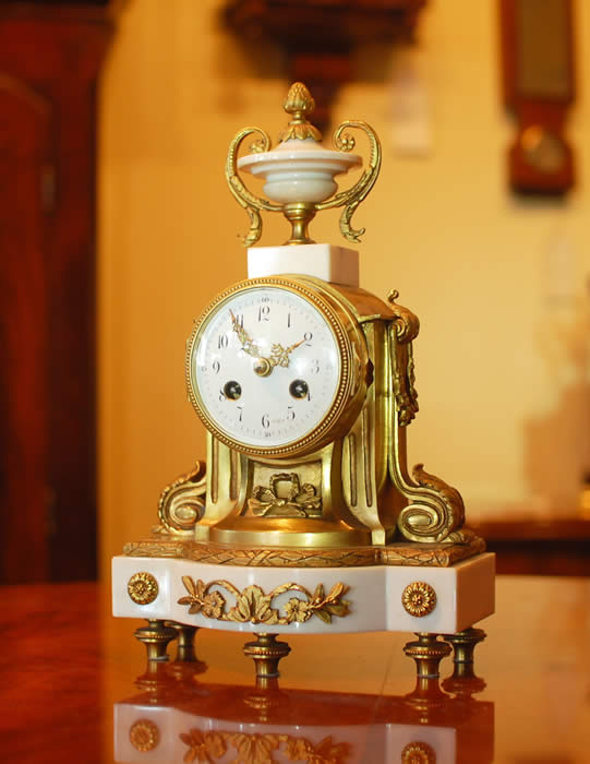 A very petite French mantel clock on a white Marble base with Ormalu case and decorations , the clock is of 8 day duration , striking hourly and half hourly on a bell with a white convex enamel dial showing arabic Numerals and finely pierced Gilded Brass Hands , and a cast brass bezel surround . This clock has a very small 
